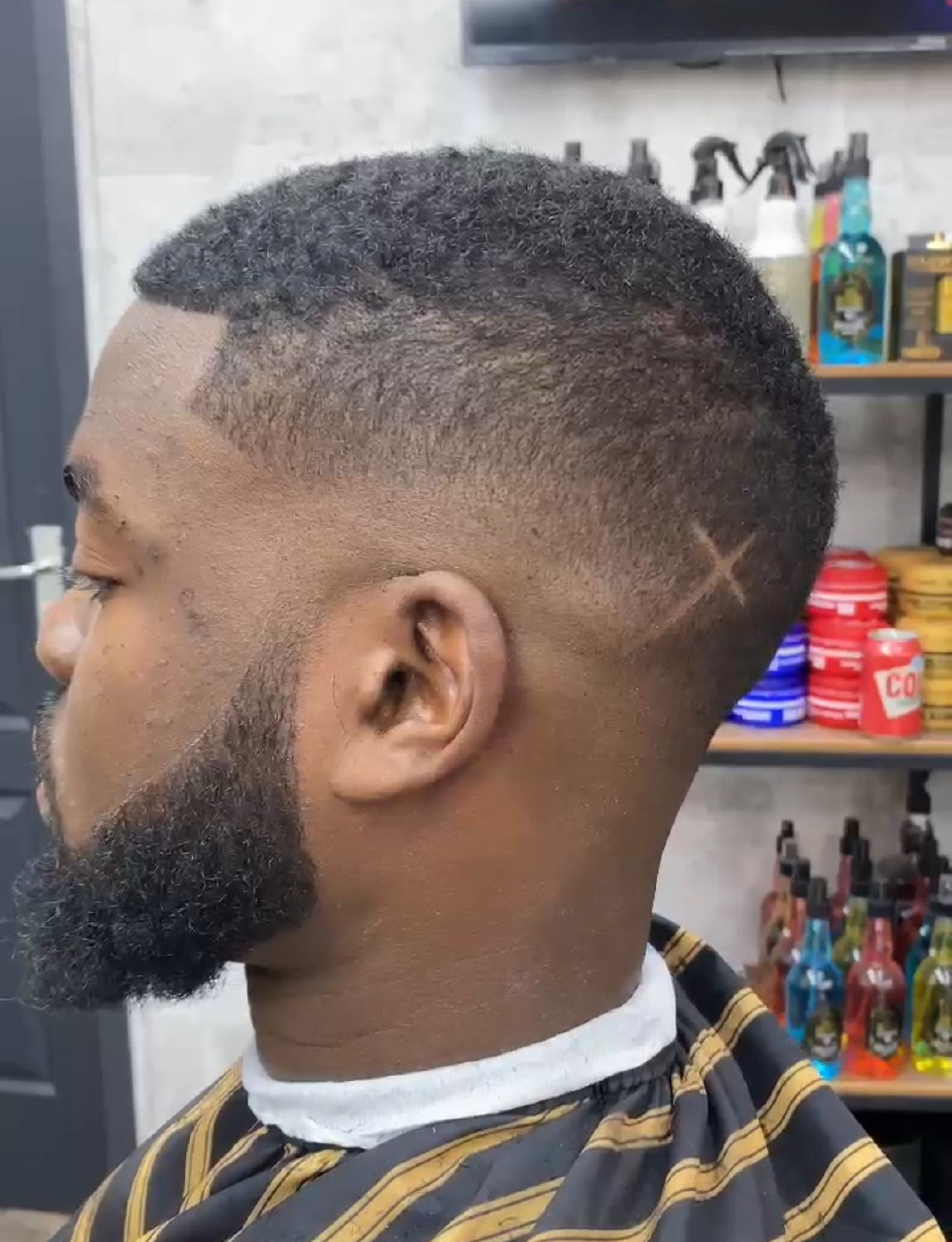 A man with a beard and shaved head getting a buzcut in a barber shop.