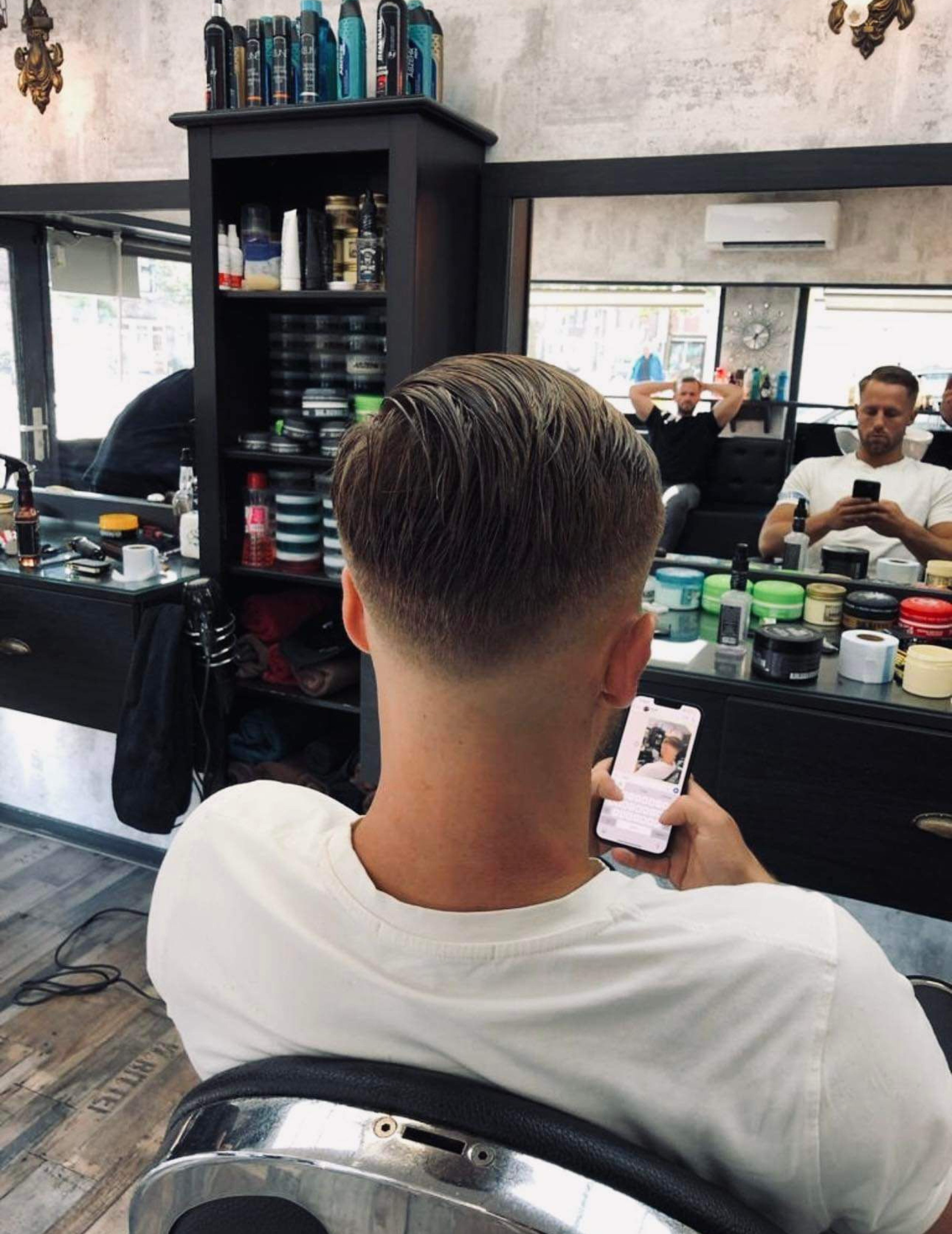 A man sitting in a barber chair looking at his phone.